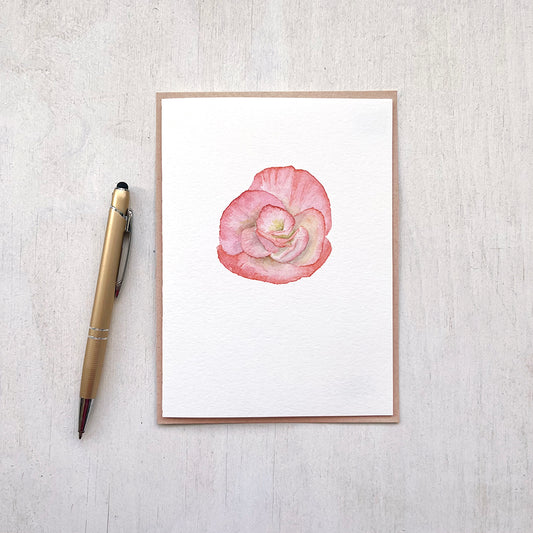 A watercolour note card featuring a delicate painting of a salmon-coloured begonia flower. Artist Kathleen Maunder.