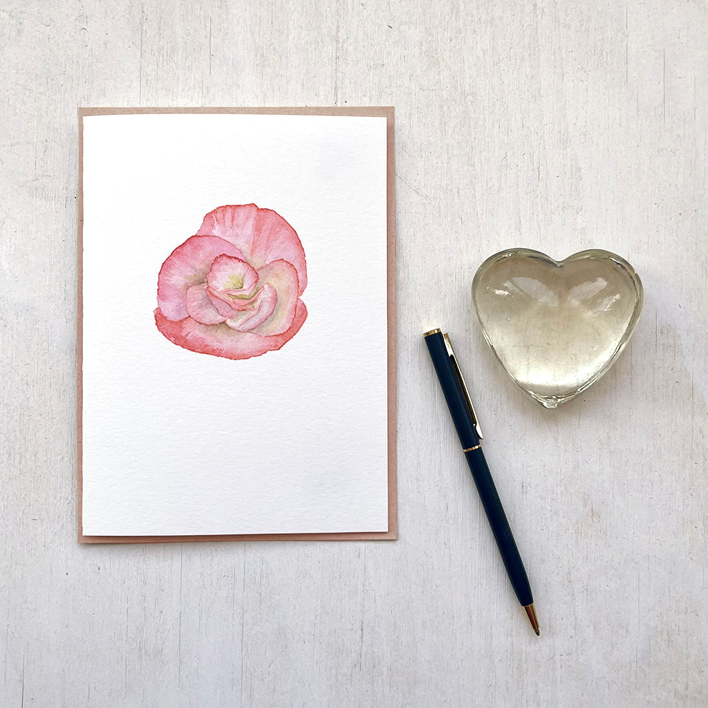 A note card featuring a delicate watercolor painting of a peach-colored begonia flower by artist Kathleen Maunder.