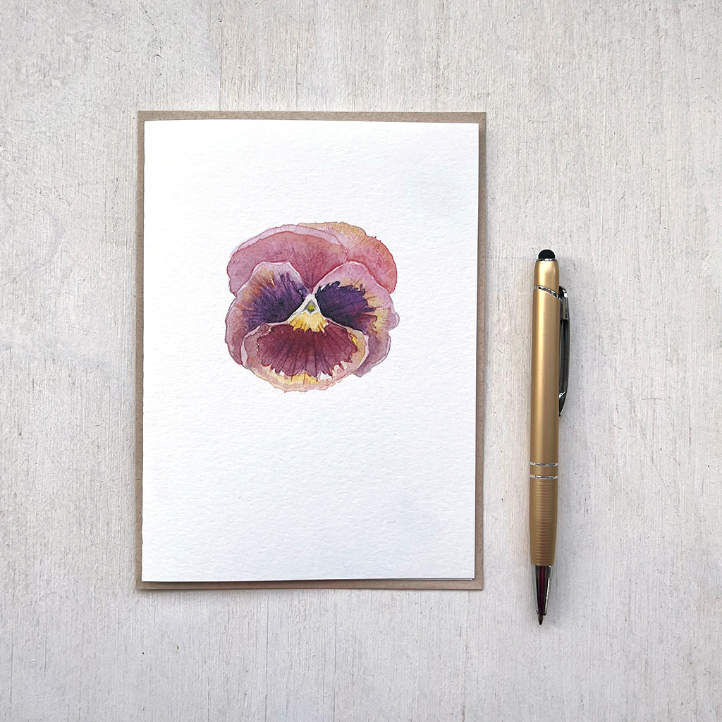 A note card with a delicate watercolour painting of a burgundy pansy. Pictured with its accompanied envelope and a pen (not included).