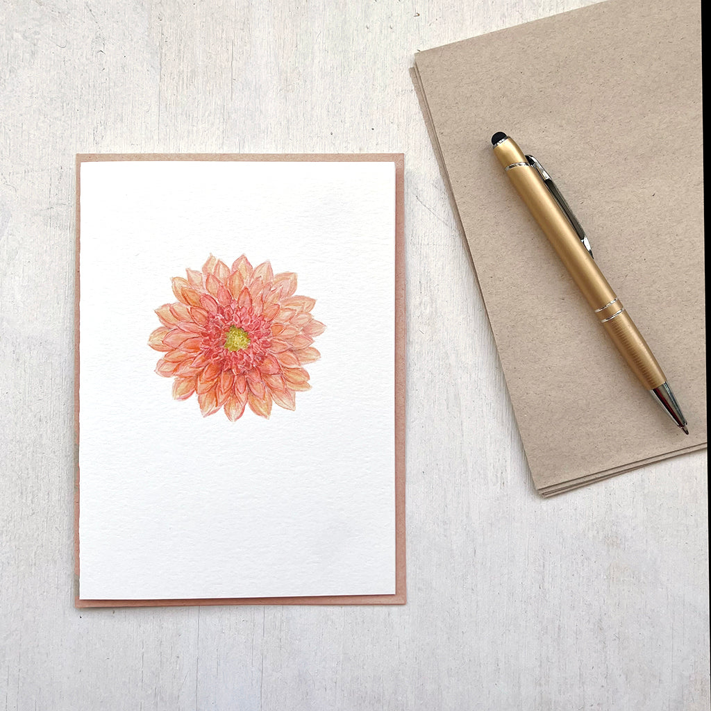 A note card featuring a watercolour painting of a coral coloured dahlia flower. Accompanied by a recycled envelope.