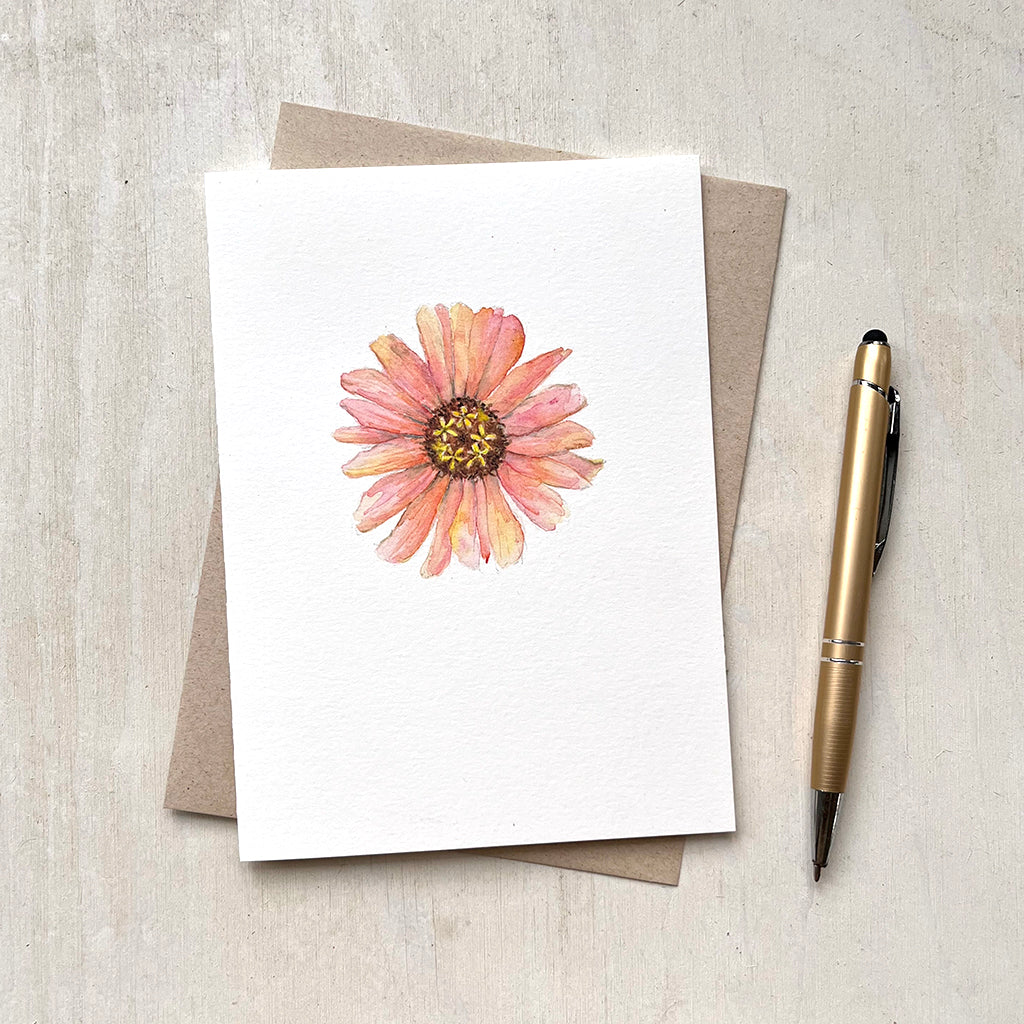 A note card with a watercolour painting of a pretty peach-coloured zinnia. Lovely tones of pink, orange and yellow. Artist Kathleen Maunder.