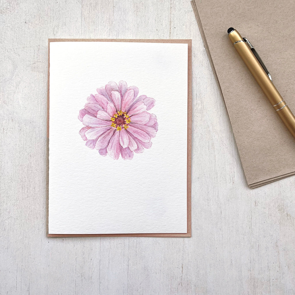 A note card featuring a beautiful pink zinnia watercolor painting is shown by its accompanying recycled envelope.